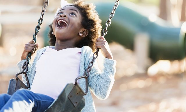 une petite fille à la peau noire se balance en riant