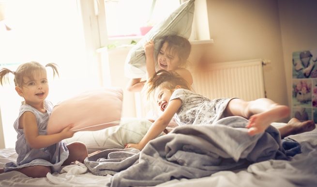 3 enfants qui font une bataille d'oreillers dans un lit