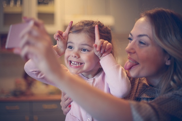 Une petite fille fait une grimace en prenant un selfie avec sa mère