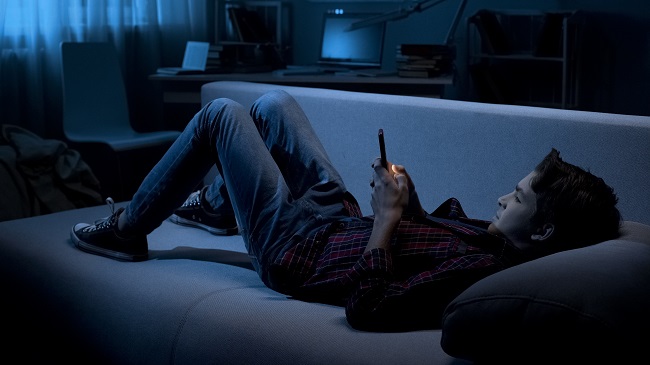 adolescent qui regarde son téléphone portable couche sur le fauteuil