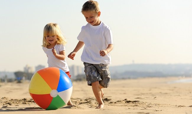 une fillette et un garcon jouent au ballon sur la plage