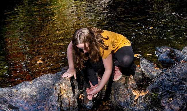 fillette qui bois de l'eau dans un ruisseau