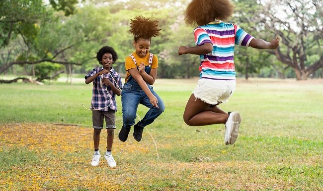 Groupe d'enfants afro-américains s'amusant à sauter par-dessus la corde dans le parc.
