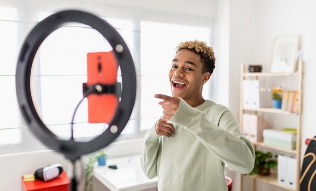 Jeune créateur masculin enregistrant une vidéo multimédia en ligne dans sa chambre