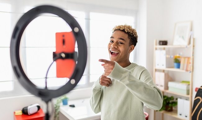 Jeune créateur masculin enregistrant une vidéo multimédia en ligne dans sa chambre