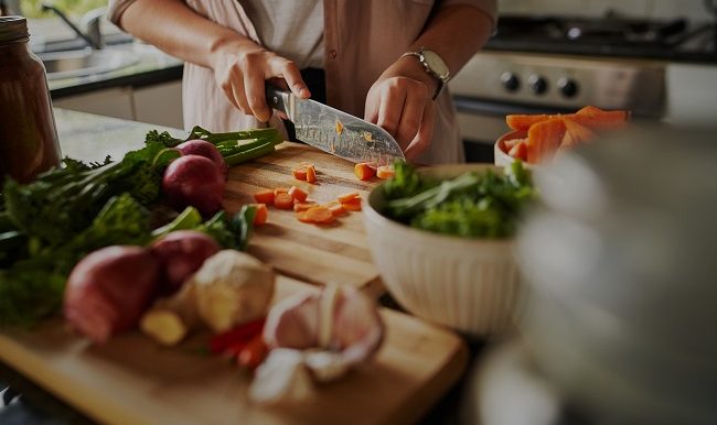 Mains féminines coupant des légumes sur une planche à découper
