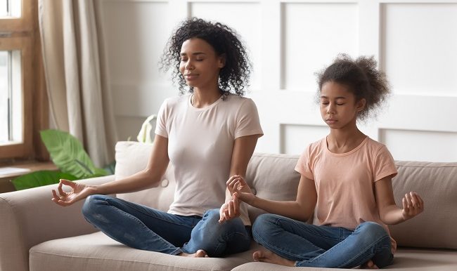 Black mother and daughter doing yoga exercises at home.