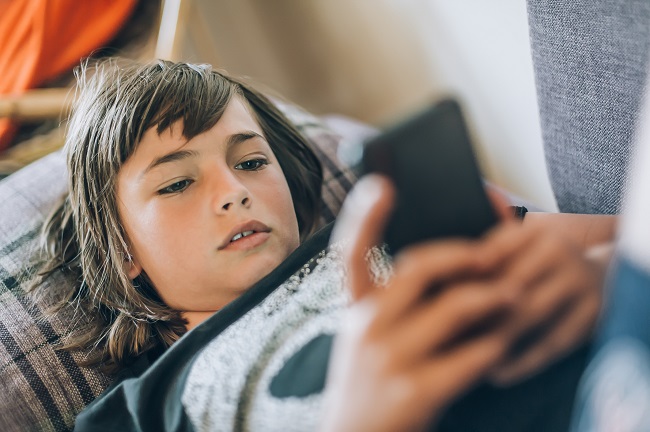 adolescent couché sur le divan qui regarde son téléphone cellulaire